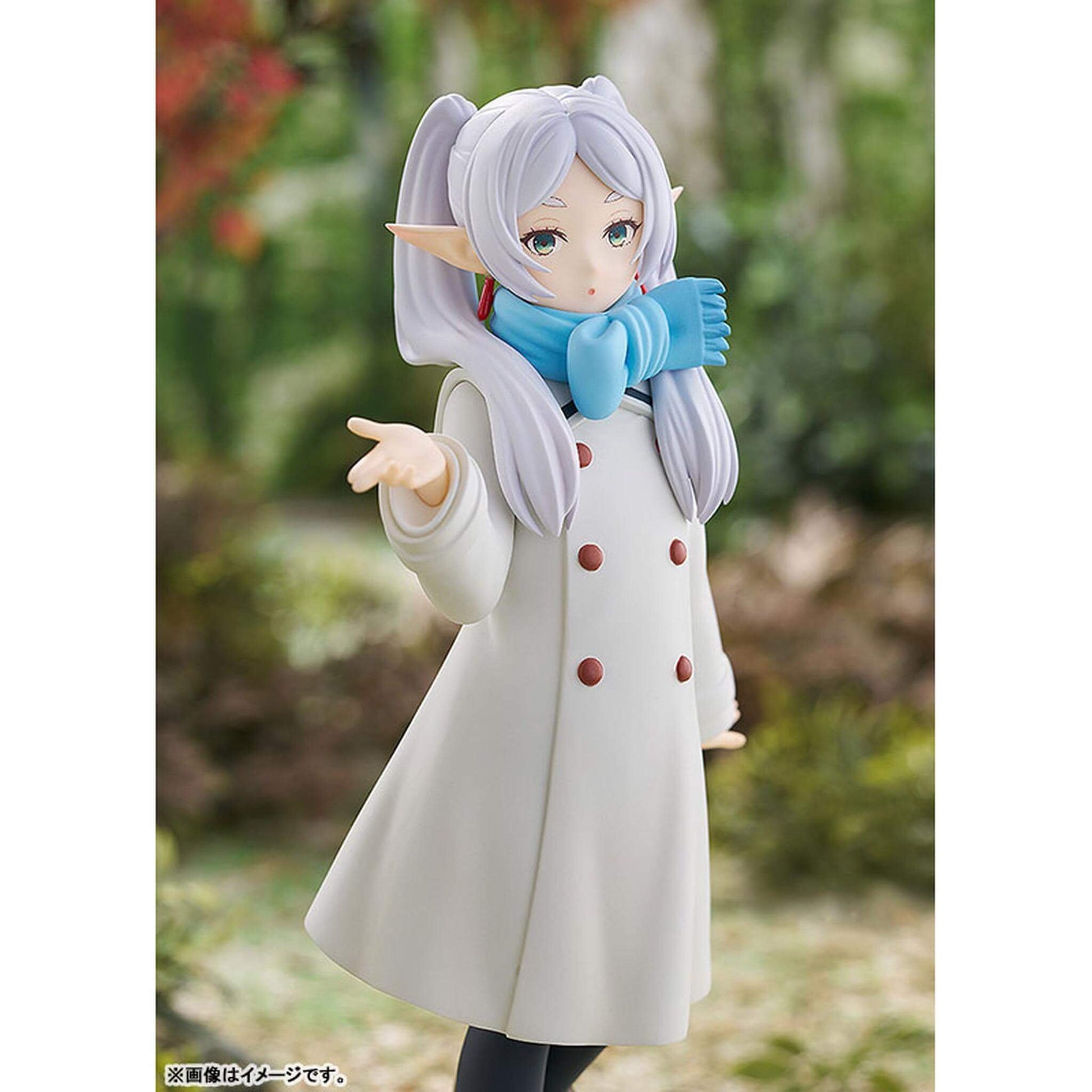 Frieren Blow Kiss Pop Up Parade figure with white hair and blue gloves, wearing a beige coat with brown buttons, against a blurred natural background.