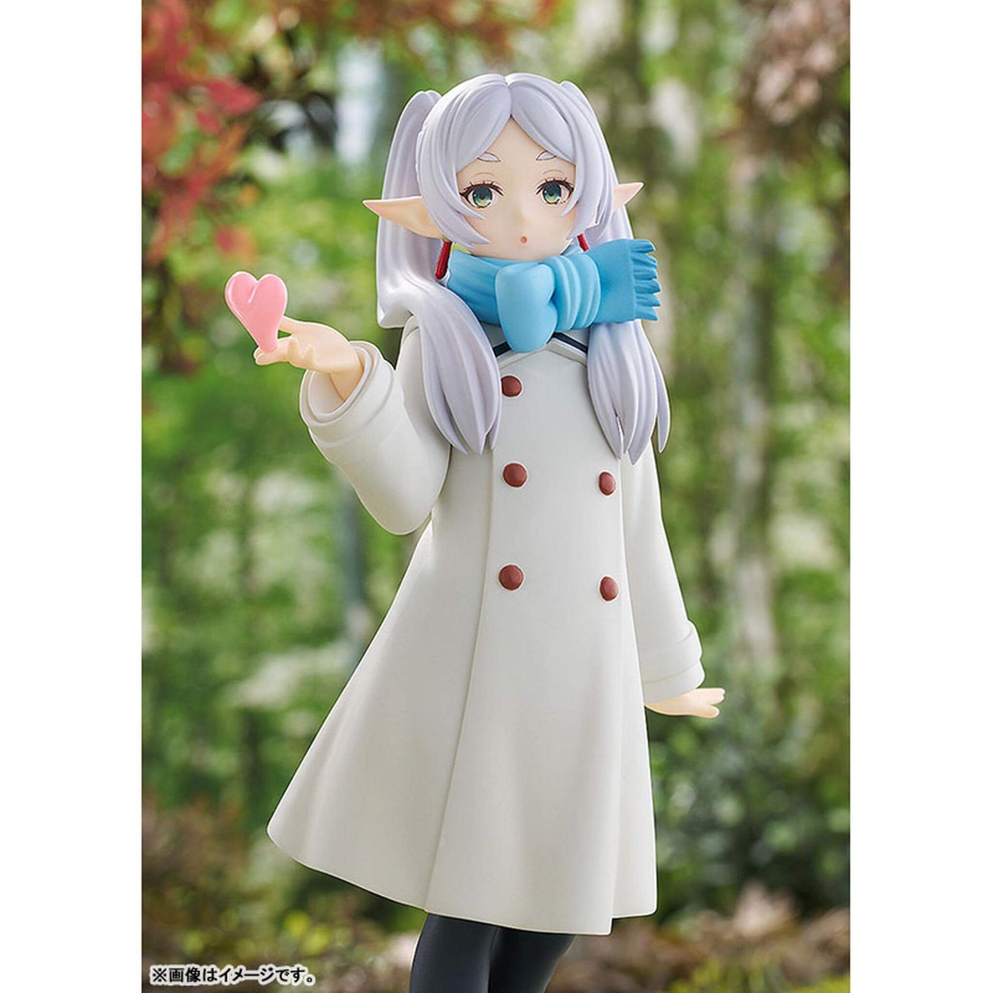 Frieren Blow Kiss Pop Up Parade figure   with white hair and blue scarf holding a pink heart, standing outdoors.