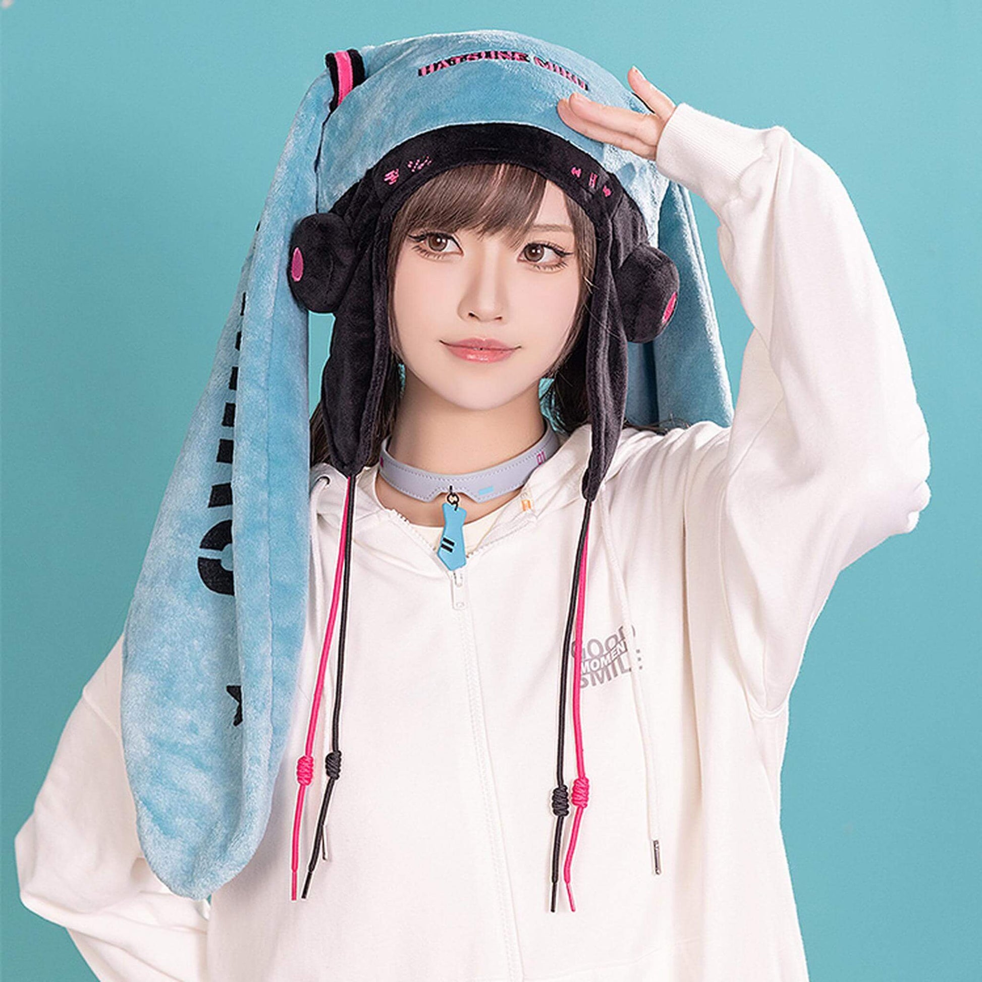 Person wearing a Hatsune Miku Character Hat with a blue hood and pink drawstrings on a teal background